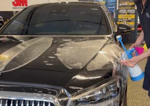 A close-up of a person applying protective film on a black car, using a spray bottle for the installation process.