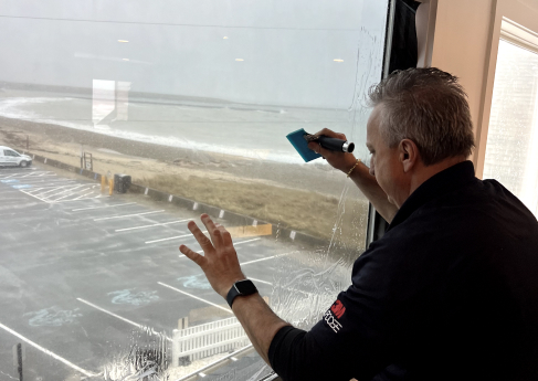 A person cleaning a large window with a squeegee, showing a beach view in the background.