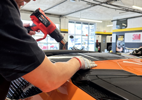 A technician using a heat gun to apply a vinyl wrap to the car’s roof.