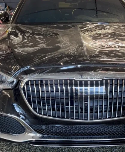 A person applying protective film on the front of a black Maybach vehicle in a professional setting.