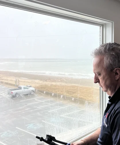 A person using a squeegee to clean a window inside a building, with a beach view in the background.