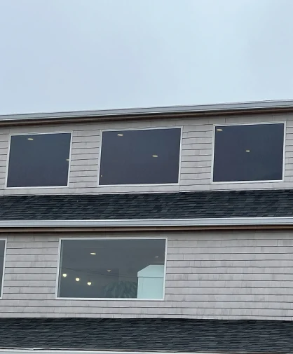 A close-up of a house with large windows on the second floor, showing a cloudy sky outside.