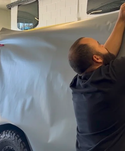 Expert applying tinting film to a large SUV, the film being pulled over the vehicle's body.